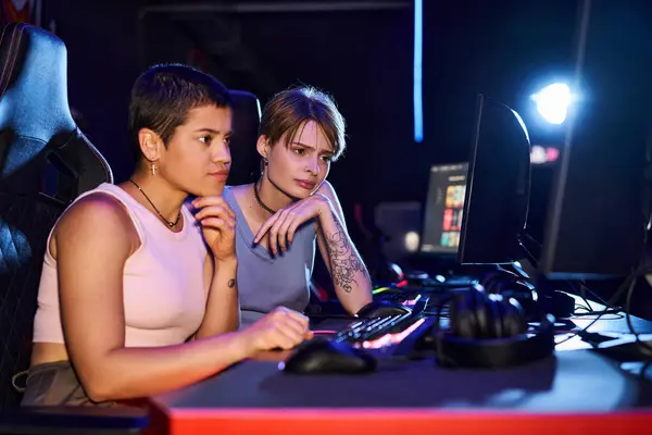 Two players sharing a station, heads close together over the keyboard as they read the screen
